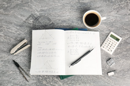 Doing homework. Notebook with math assignment, coffee and stationery on grey desk, flat lay