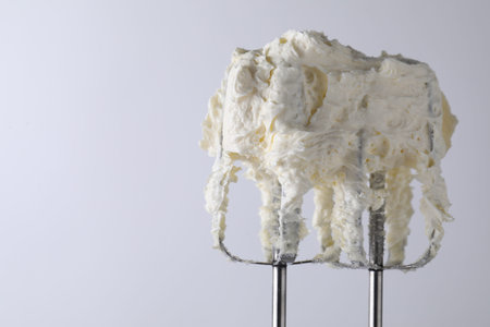 Whisks with whipped cream on white background, closeup. Space for text