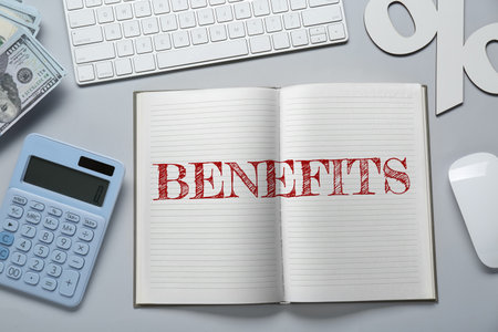 Benefits word in notebook, calculator, money, computer keyboard and mouse on gray table, top viewの写真素材