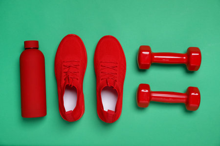 Dumbbells, water bottle and sneakers on green background, flat lay