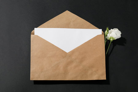 Kraft paper envelope with letter and flower on black background, above view. Mockup for designの写真素材