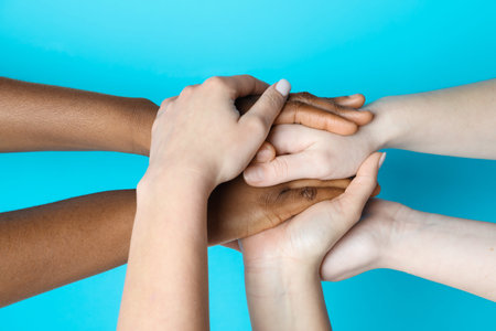 Stop racism. People of different skin colors joining hands on light blue background, closeup