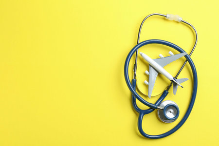 Medical tourism. Stethoscope and plane model on yellow background, flat lay. Space for textの写真素材