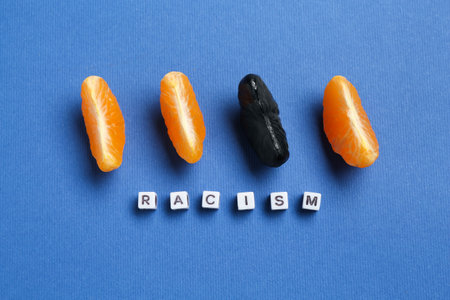Word Racism and tangerine segments of different colors on blue background, flat lay