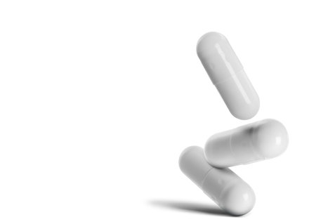 Three medical pills falling on white backgroundの写真素材