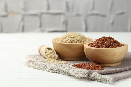 Different types of brown rice in bowls and scoop on white wooden table, closeup. Space for textの写真素材