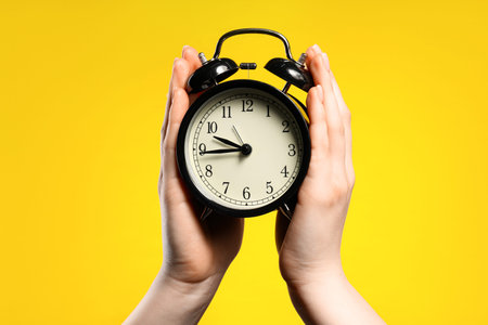 Woman with black alarm clock on yellow background, closeupの写真素材