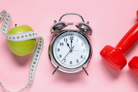 Alarm clock, dumbbells, apple and measuring tape on pink background, flat layの写真素材