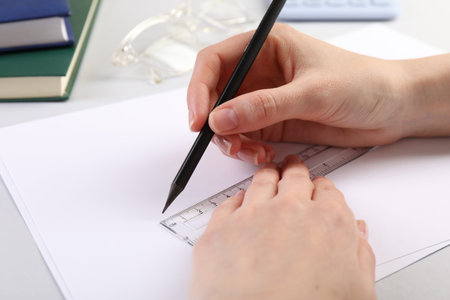 Woman drawing sketch with ruler and pencil on paper at white table, closeup