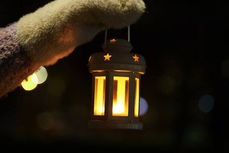 Woman holding Christmas lantern with burning candle in darkness, closeup. Space for textの写真素材
