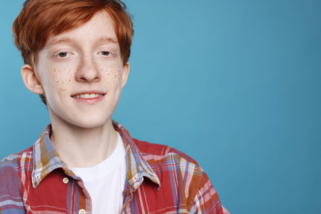 Smiling teenage boy with freckles on light blue background. Space for textの写真素材