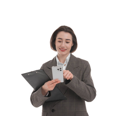 Smiling secretary with clipboard using smartphone on white backgroundの写真素材
