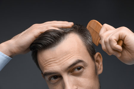 Handsome man combing his hair on dark background, closeupの写真素材