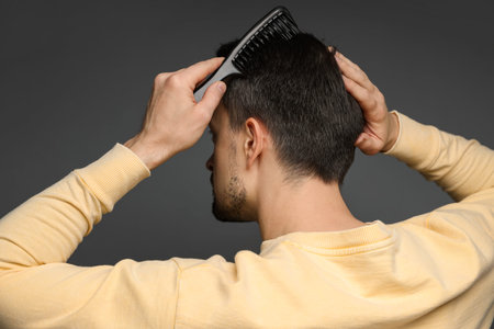 Man combing his hair on dark background, back viewの写真素材
