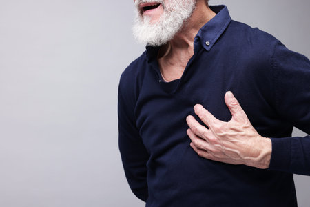 Heart attack. Senior man suffering from pain in chest on grey background, closeup. Space for text