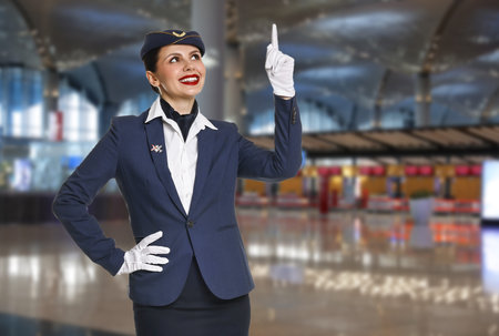 Smiling stewardess pointing upwards in airport terminal.