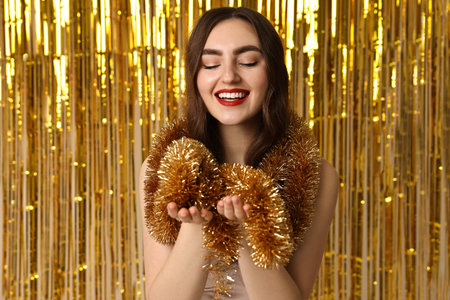 Happy young woman with tinsel against golden foil curtainの写真素材