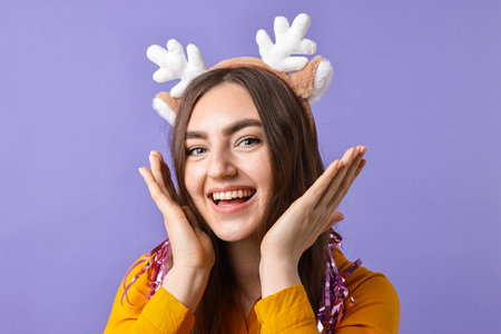 Happy young woman in reindeer headband with tinsel on purple backgroundの写真素材