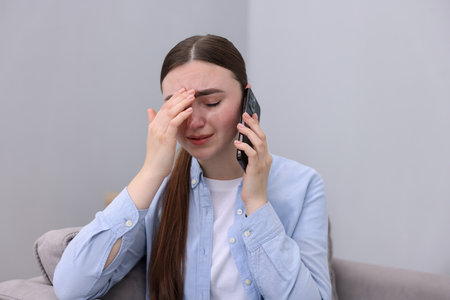 Stressed woman calling hotline for mental health help in armchair at homeの写真素材