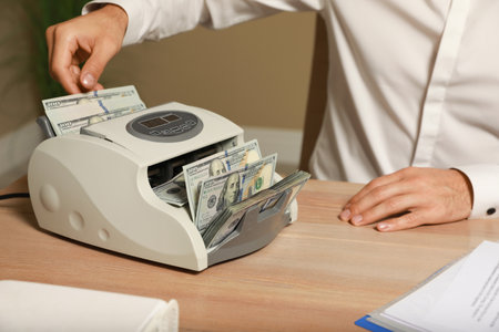 Man putting money into banknote counter at wooden table indoors, closeupの写真素材