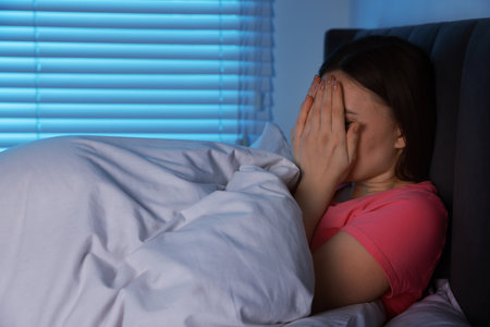 Fear of darkness. Scared young woman lying on bed in room at night, space for textの写真素材