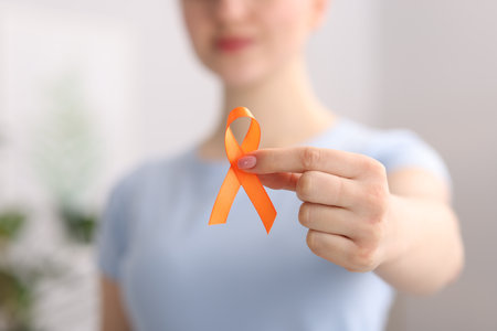 Multiple Sclerosis awareness. Young woman holding orange ribbon indoors, closeupの写真素材