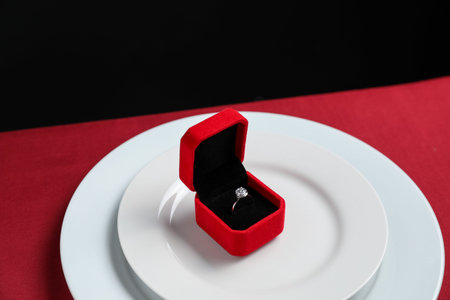 Beautiful engagement ring and setting for romantic dinner on red table, closeup