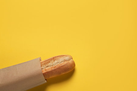 Paper bag with fresh baguette on yellow background, top view. Space for textの写真素材