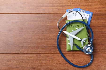 Medical tourism. Passport with tickets, stethoscope and airplane model on wooden background, top view. Space for textの写真素材