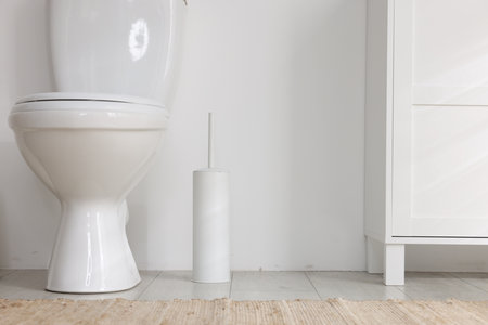 Toilet and brush on floor near white wallの写真素材