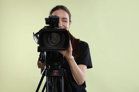 Woman with professional video camera on pale olive background