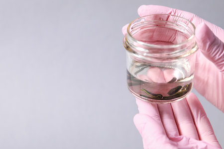Woman holding glass jar with medicinal leeches on gray background, closeup.の写真素材