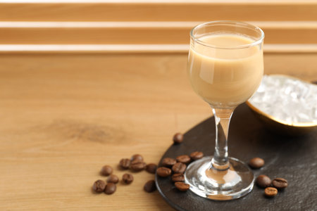 Coffee cream liqueur in glass, ice and beans on wooden table, closeup. Space for text