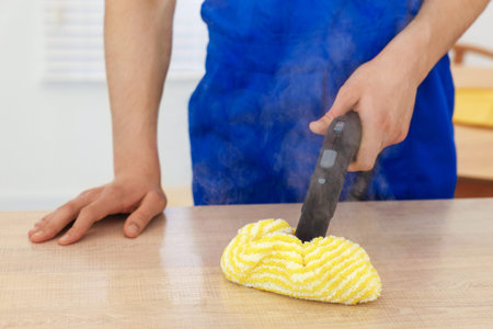 Janitor cleaning wooden surface with steam cleaner at home, closeup
