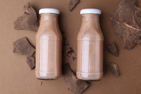 Tasty chocolate milk in glass bottles and pieces of chocolate on brown background, flat layの写真素材