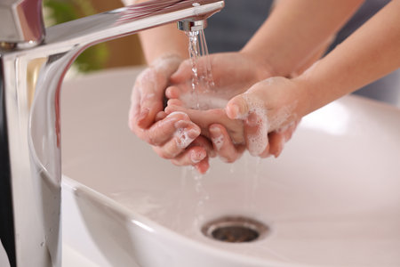 Mother and daughter washing their hands above sink indoors, closeupの写真素材