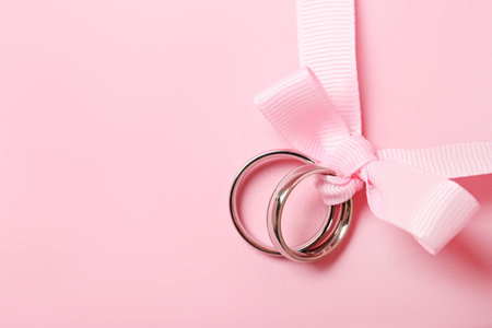 Wedding rings tied with ribbon on pink background, top view. Space for textの写真素材