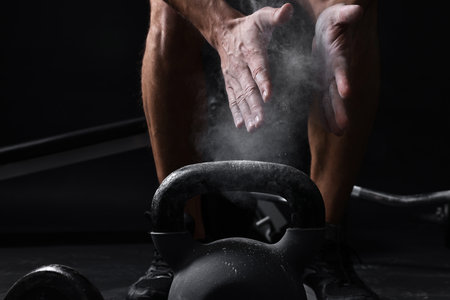 Man clapping hands with powder before training with kettlebell on black background, closeupの写真素材