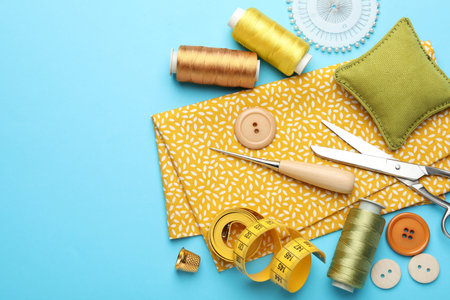 Different sewing supplies on light blue background, flat lay.
