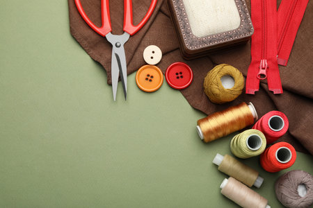 Different sewing supplies on olive background, flat lay. Space for text