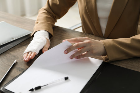 Woman with medical bandage on her wrist working at wooden table indoors, closeupの写真素材