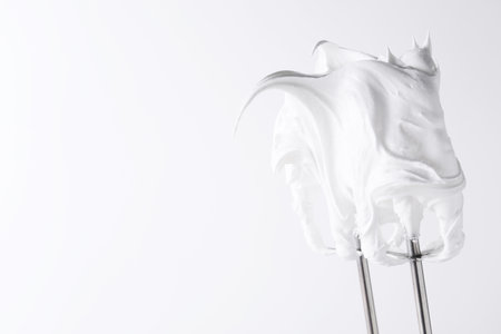 Whisks with whipped cream on white background, closeup. Space for textの写真素材