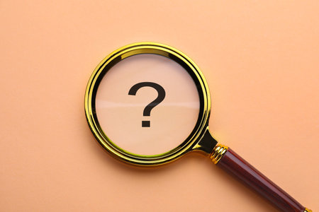 Question mark on peach color background, top view through magnifying glassの写真素材