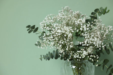 Beautiful gypsophila flowers and eucalyptus branches in vase on turquoise background, closeup. Space for textの写真素材