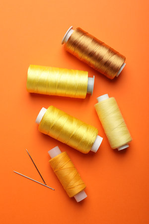 Spools of thread and needles on orange background, flat layの写真素材