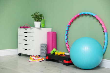Different fitness equipment, sneakers and chest of drawers near green wall indoorsの写真素材