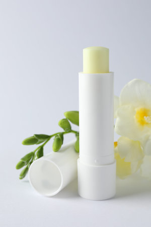 Lip balm and freesia flowers on white background, closeup