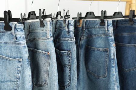 Many stylish jeans hanging from rack on white background, closeupの写真素材