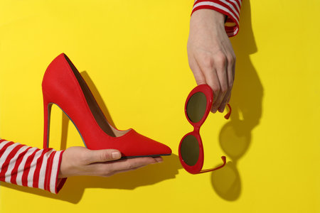 Woman showing red high-heeled shoe and sunglasses on yellow background, closeupの写真素材