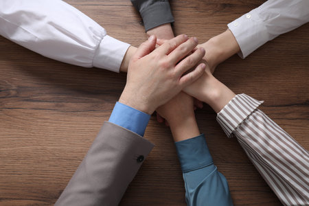 Business concept. Group of people stacking hands at wooden table, top view